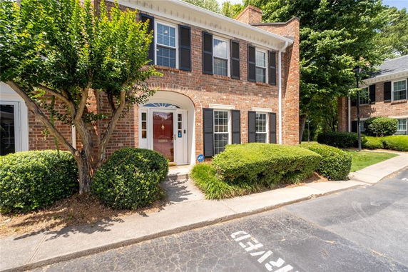 Front view of a two-story brick townhouse with black shutters and a white entryway.