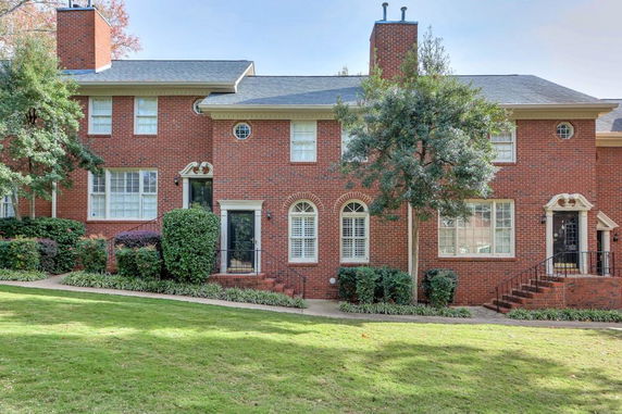 Front view of a two-story brick townhouse with arched windows and chimneys.