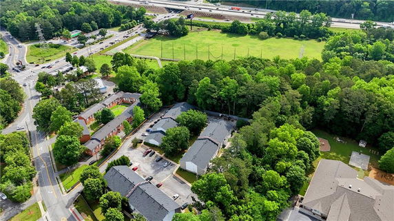 Aerial view showing buildings surrounded by trees and roads, with a highway and open field in the background.