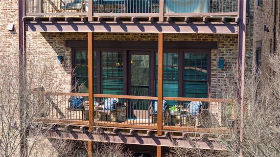 Balcony view of a brick building with wooden railing and outdoor seating.