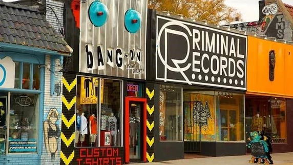Street view of shops with colorful and artistic storefronts, including a T-shirt store and a record store.