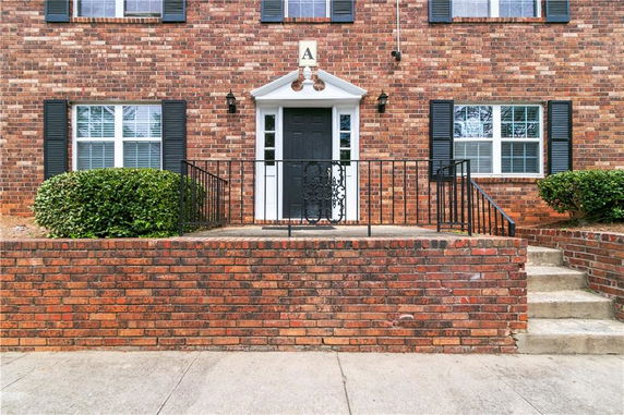 Front view of a brick building entrance with black door and shutters.