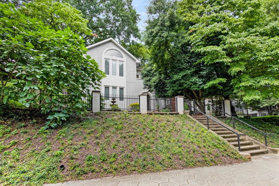 Front view of a two-story house with a steep walkway and surrounding trees.