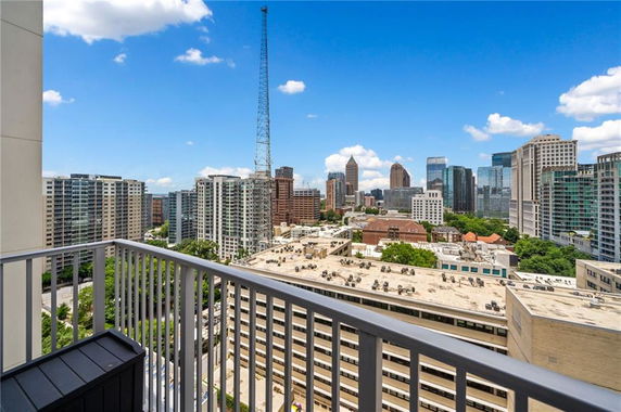Panoramic view of a cityscape from a balcony, featuring several high-rise buildings and a clear blue sky.