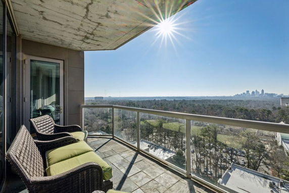 Panoramic view from a balcony overlooking a city skyline and forested area.