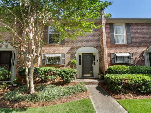 Front view of a two-story brick townhouse with dark shutters and a landscaped entrance.