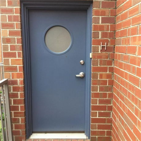 Exterior view of a blue door with a circular window on a brick wall.
