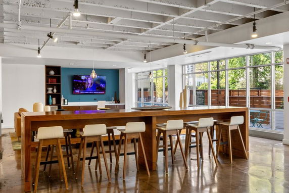 Interior view of a recreation area with barstools, wooden tables, and a television mounted on the wall.