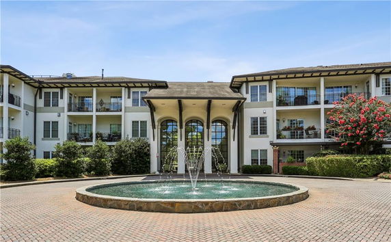 Front view of a multi-story building with balconies and a central entrance, flanked by a circular fountain.
