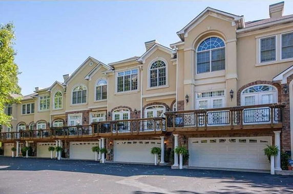 Front view of a row of three-story townhouses with a uniform exterior design and garages at the ground level.