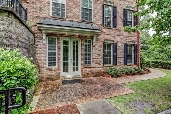 Front view of a brick two-story house with French doors and black shutters.