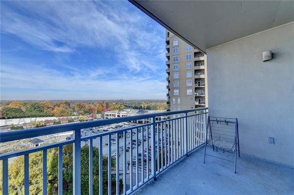 Balcony view overlooking a parking area and distant trees with a cityscape.
