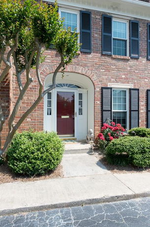 Front view of a brick house with white windows and a red door.