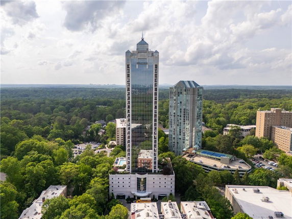Front view of a tall skyscraper set among other buildings with a forested area in the background.