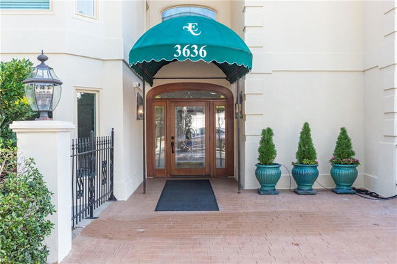 Entrance of a building with a green awning and decorative potted plants.