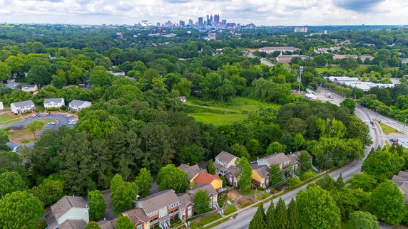 Aerial panoramic view of suburban neighborhood with trees and distant city skyline.