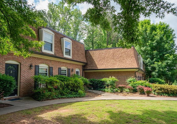Front view of a two-story brick house with dormer windows and a brown shingled roof.