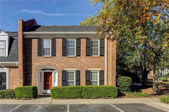 Front view of a two-story brick house with a red door and black shutters.