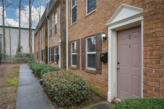 Front view of a brick townhouse with a light pink door and brown shutters.
