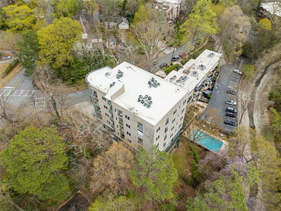 Aerial view of a multi-story building with a flat rooftop featuring multiple small rooftop units surrounded by trees and greenery.