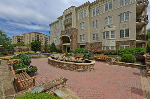 Front view of a multi-story residential building with a landscaped garden and a small fountain.