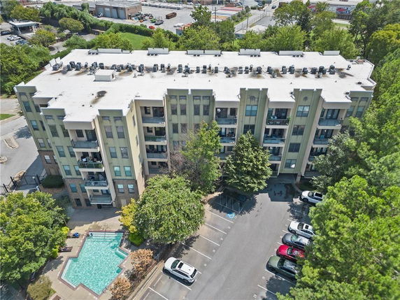 Aerial view of a multi-story residential building with balconies and a flat roof, adjacent to a parking area and swimming pool.
