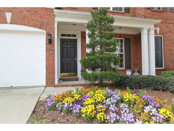 Front view of a brick house with a columned entrance and flowers.