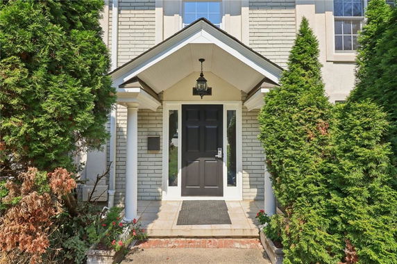 Front entrance of a house with black door and porch pillars.