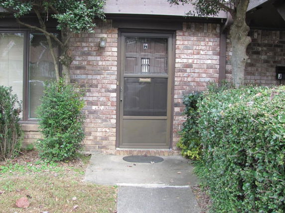 Front view of a brick house entrance with a screen door and adjacent windows.