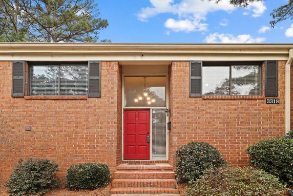 Front view of a brick house with a red door and large windows.
