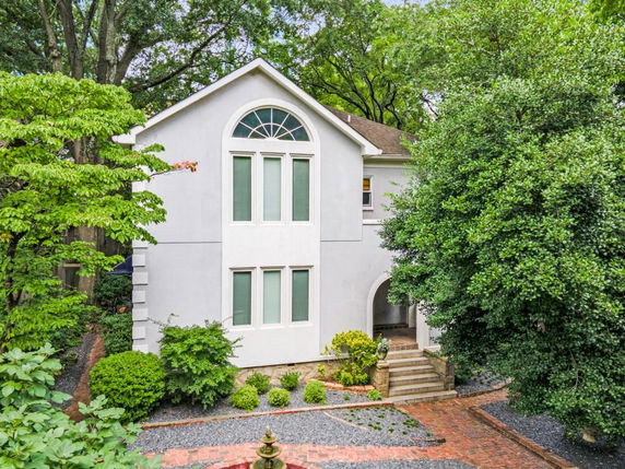 Front view of a two-story house with arched windows and an entryway surrounded by trees and shrubs.