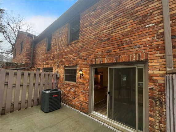 Rear view of a two-story brick house with sliding glass doors and a fence.
