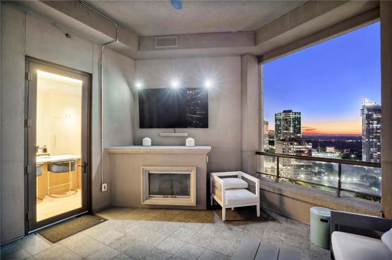 Outdoor seating area with a fireplace and TV, overlooking a cityscape during sunset.