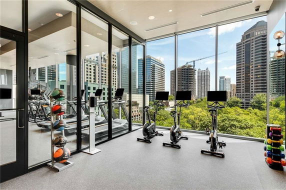 Modern gym area with exercise bikes, treadmills, and large glass windows offering a city view.