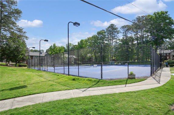 Outdoor tennis court with surrounding fence and lights.