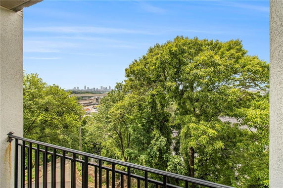 Panoramic view from a building balcony showing trees and a distant city skyline.