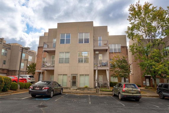 Front view of a multi-story building with balconies and parking area in front.