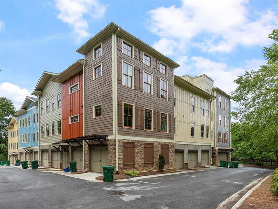 Front view of a multi-story residential building with a variety of siding colors and multiple garage entrances on the ground level.
