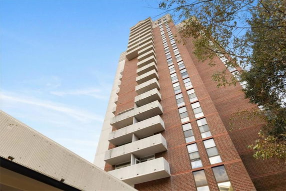 View of a tall brick residential building with multiple balconies.