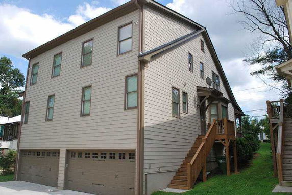 Side view of a multi-story house with an external staircase and three garage doors.