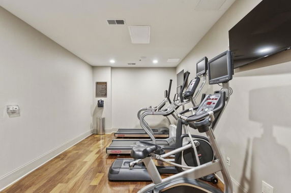 Indoor gym area with multiple exercise machines and wall-mounted TVs.