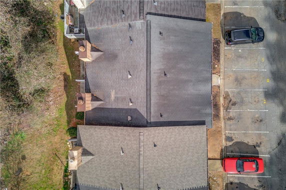 Aerial view of a building rooftop with visible chimneys and nearby parking area.