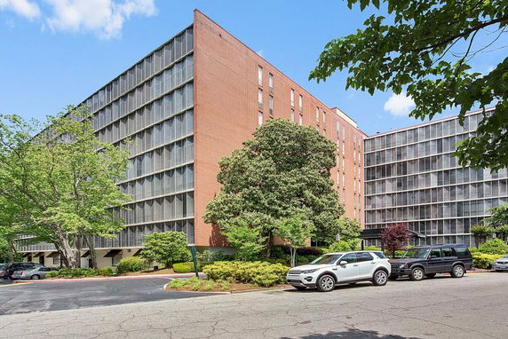 Front view of a multi-story brick building with large windows and parking area.