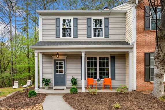 Front view of a two-story house with a porch and chairs.