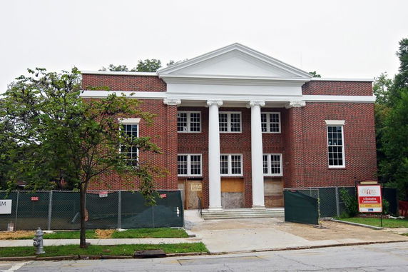 Front view of a brick building under construction with large columns and a triangular pediment.