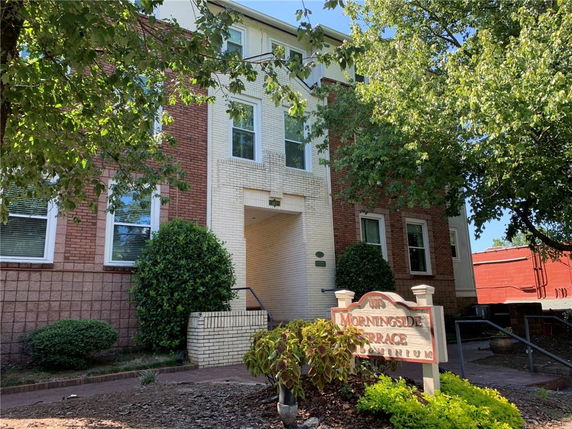 Front view of a multi-story brick condominium building with trees in the foreground.