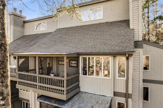 Front view of a multi-story house with grey siding and a sloped roof, featuring a large balcony.