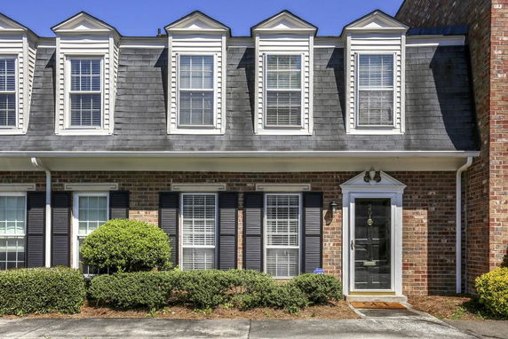 Front view of a brick townhouse with dormer windows and black shutters.