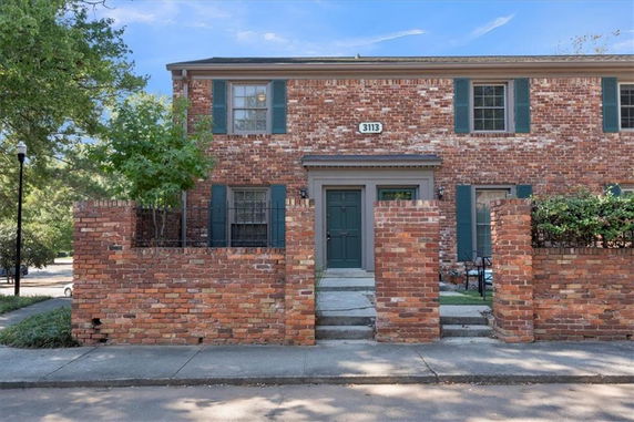 Front view of a two-story brick house with a gated brick wall.