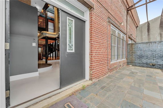 View of a brick building exterior with an open door leading into an industrial-style interior.